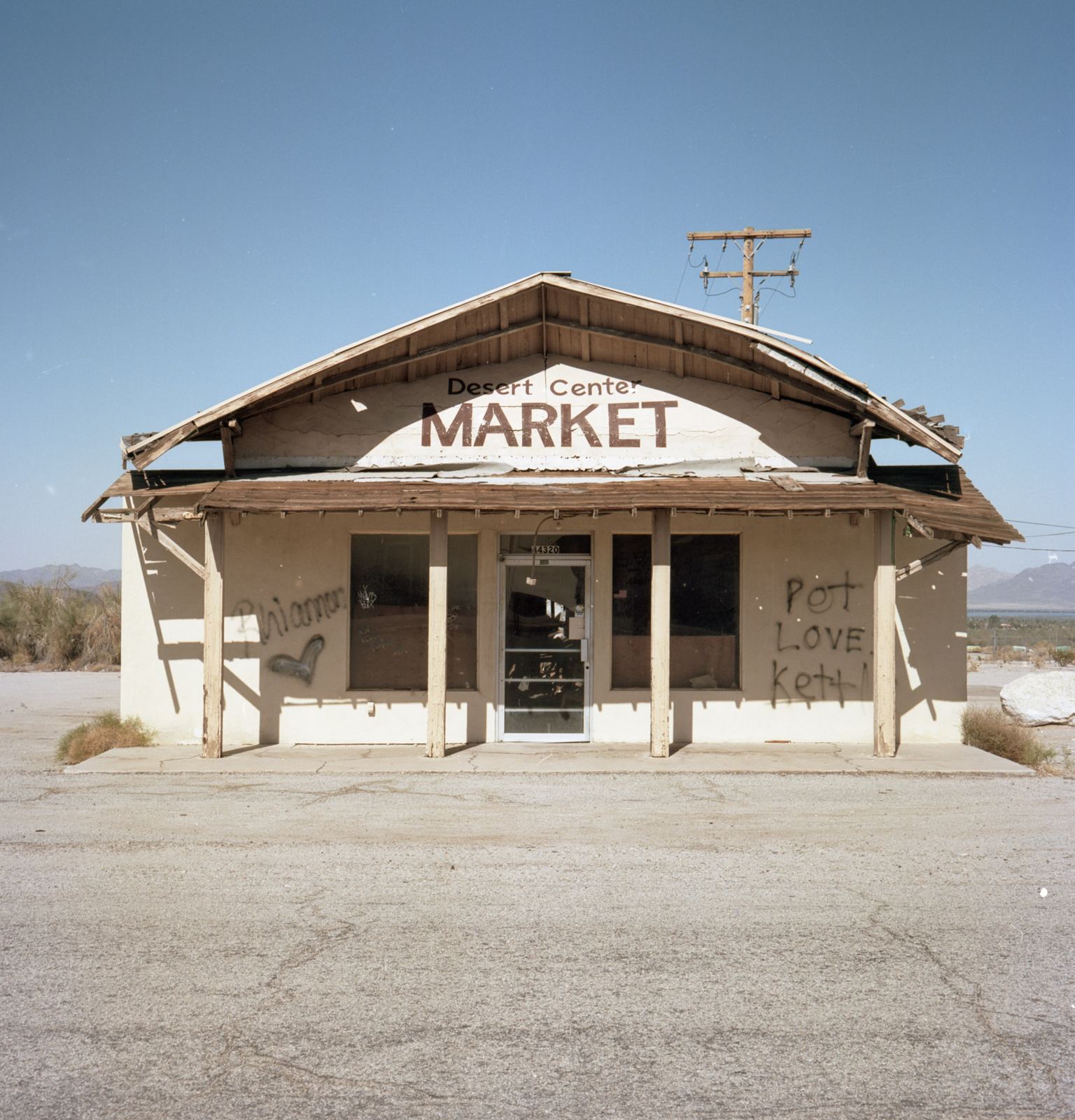 Shuttered roadside market building alone in flat desert light.