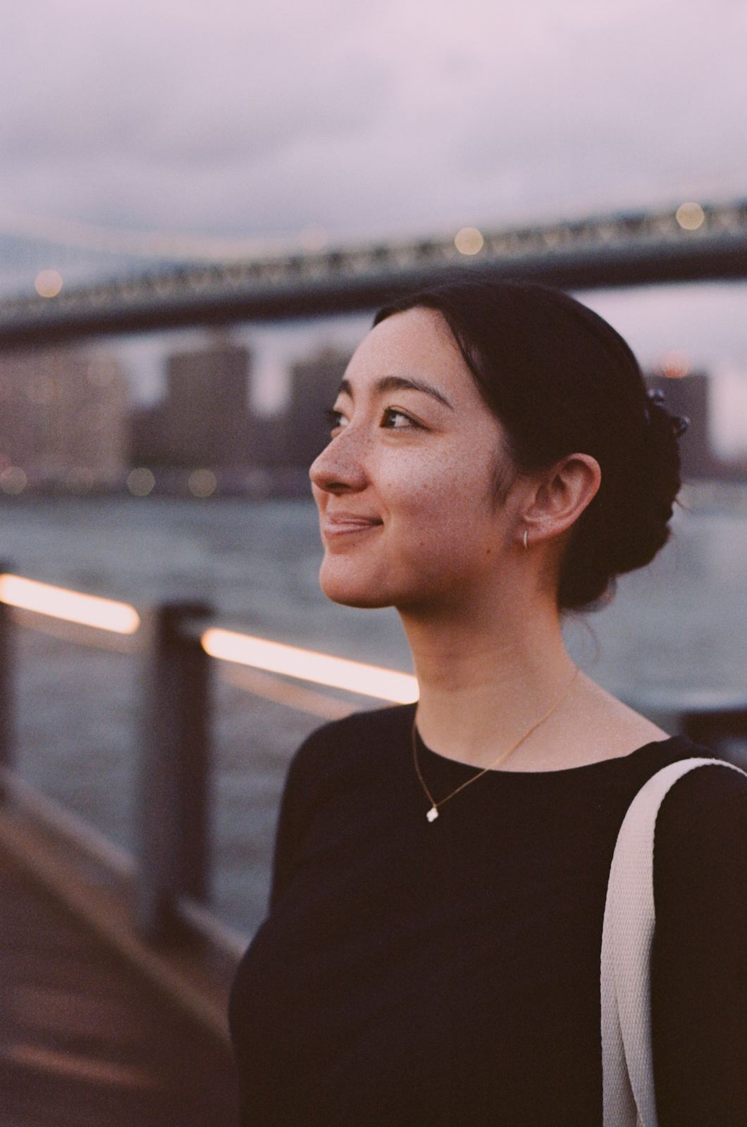 Woman looking out over the East River with a bridge behind her.